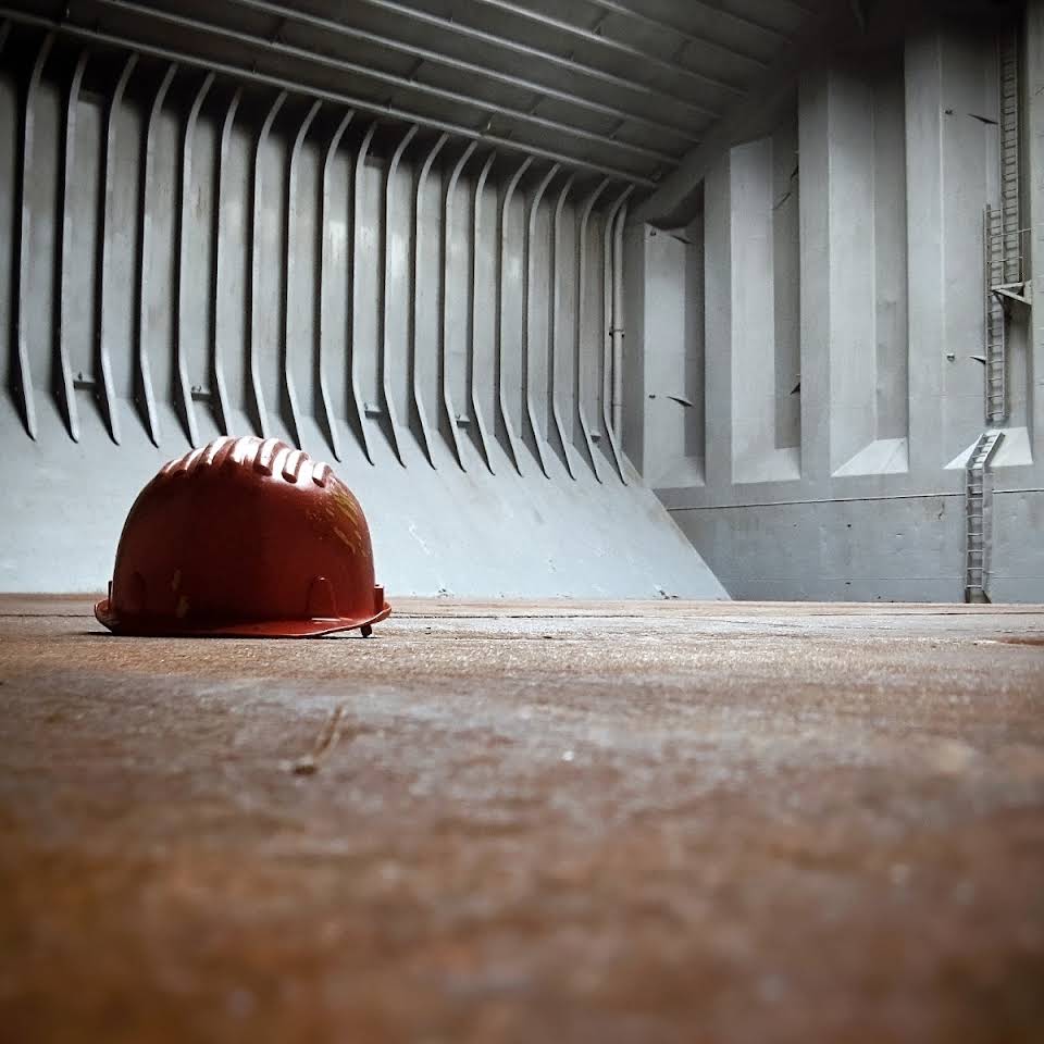 Empty ship cargo hold with ribbed steel walls and a red hard hat resting on the floor